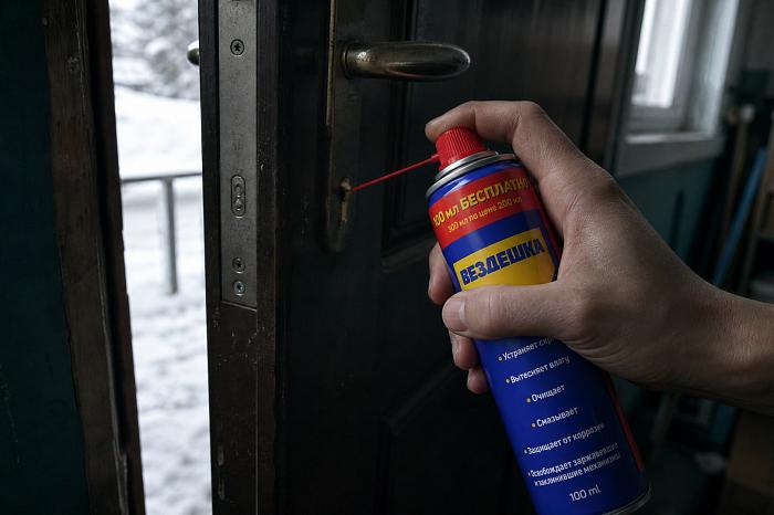 Рука в перчатке наносит универсальную смазку WD-40 на замок.